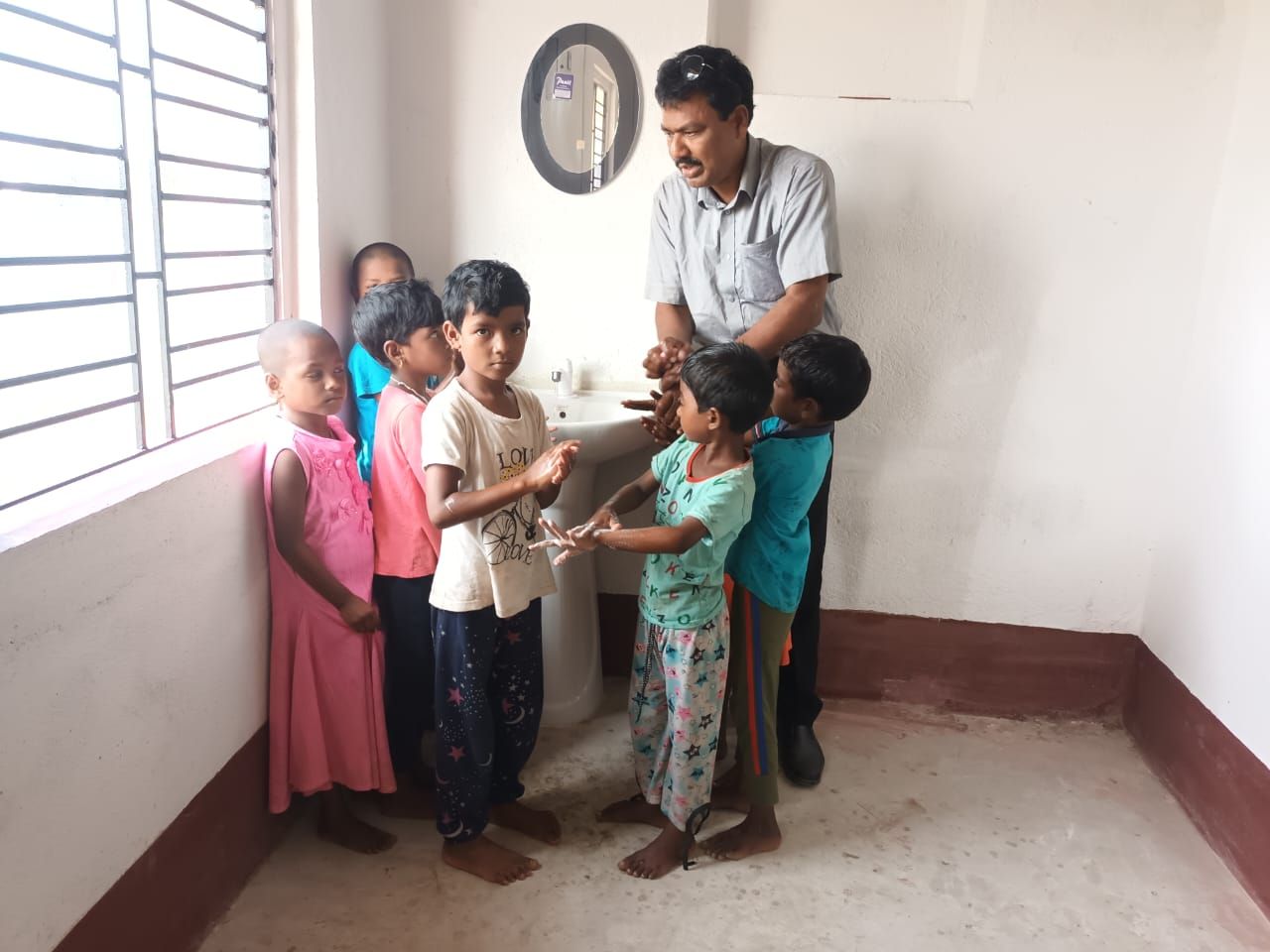 A volunteer demonstrating hand-washing steps to a small group of children