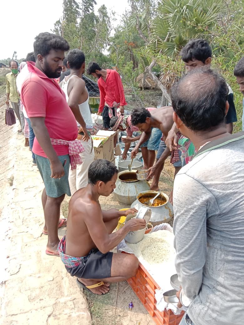 A volunteer ladling food from a pot while others wait