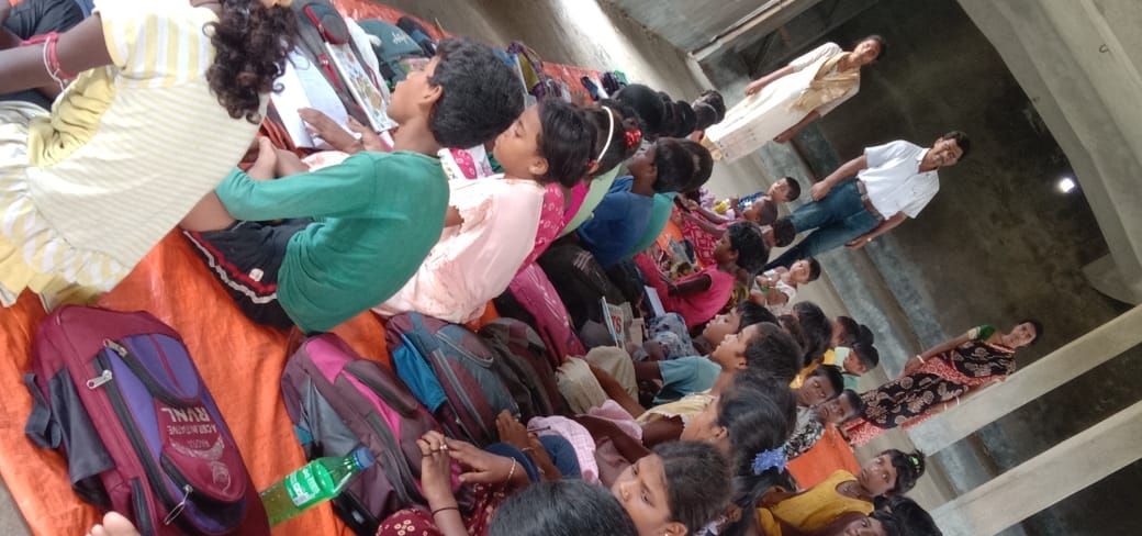 Students sitting on mats in a hall holding new school bags